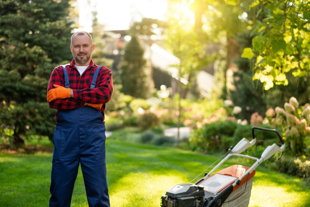 Person in Gärtnerkleidung mit Rasenmäher in einem Garten.